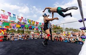A crowd watches Mexican wrestling as one wrestler flies through the air towards the other